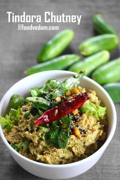 a white bowl filled with food next to green beans and coriant leaves on the side