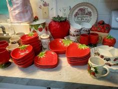 a kitchen counter topped with lots of red plates and bowls filled with strawberries on them