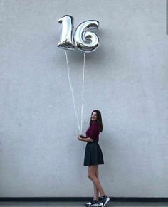 a woman holding two balloons in the shape of the letter ig and standing against a wall