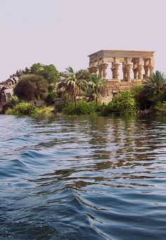 an island in the middle of water with columns on it and palm trees near by