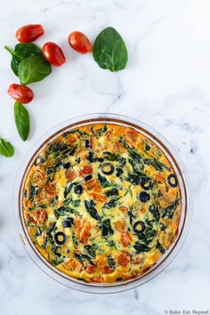 an overhead view of a quiche with spinach, tomatoes and olives on the side