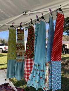 several different colored dresses hanging from a line under a tent