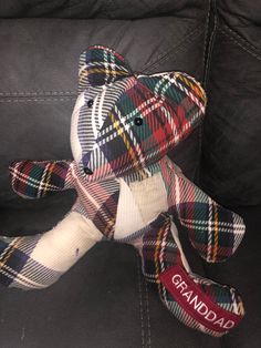 a plaid teddy bear sitting on top of a black leather couch next to a red and white tag