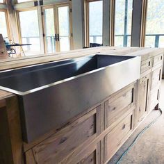 a large stainless steel kitchen sink sitting on top of a wooden counter next to windows