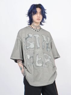 a young man with blue hair and piercings wearing a grey t - shirt that says,