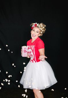 a woman in a red shirt and white tutu skirt holding a box of popcorn