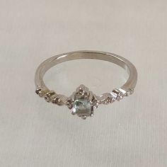 a white gold ring with an aquamarine colored stone surrounded by small diamonds on a plain surface