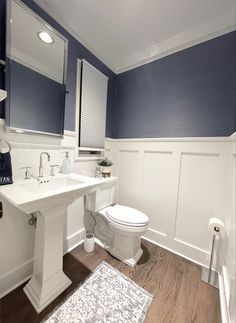 a white toilet sitting next to a sink in a bathroom on top of a hard wood floor