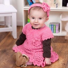 a baby sitting on the floor wearing a pink dress