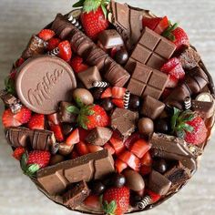 a chocolate cake with strawberries, chocolate bars and other toppings on the top