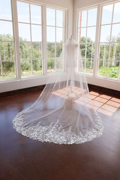 a wedding dress is hanging in the corner of a room with large windows and wooden flooring