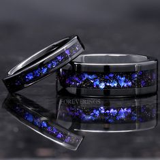 two wedding bands with blue and purple stars inlayed to each other on a black surface