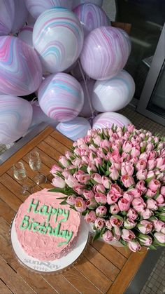 a birthday cake with pink flowers on a table next to some balloons and wine glasses