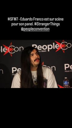 a man with long black hair sitting in front of a microphone and wearing a white shirt