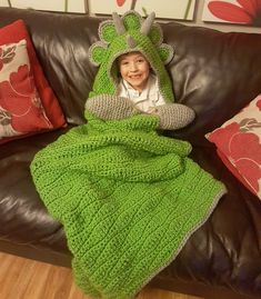 a little boy wrapped up in a green crocheted blanket on a brown couch