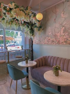 the interior of a restaurant with pastel colored furniture and flowers on the wall behind it