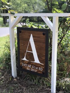 a sign that is in the grass near some bushes and trees with a tree behind it