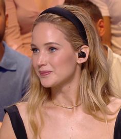 a woman with ear buds on her head smiling at the camera while people watch in the background