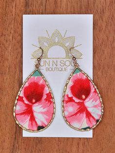 a pair of pink and red flower earrings on top of a wooden table next to a card