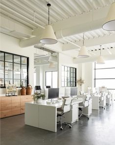 an office with white desks and chairs in front of two large windows on the wall