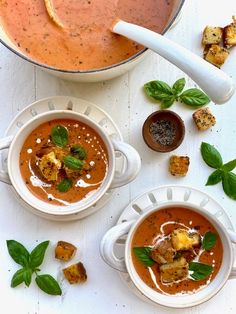 two bowls of tomato soup with basil garnishes and bread croutons