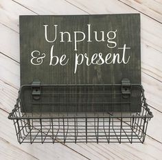 a sign that says unplug and be present hanging from a wire basket on a wooden wall