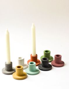 several different colored candles sitting next to each other on a white surface with one lit candle in the middle