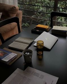 a table with books, glasses and an open laptop on it next to a window