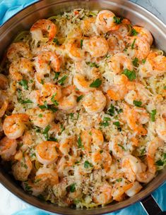 a pan filled with shrimp and rice on top of a blue table cloth next to a spoon