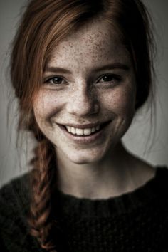 a smiling woman with freckles on her face and red hair is looking at the camera