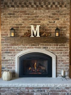 a brick fireplace with the letter m above it and two pumpkins on the mantle