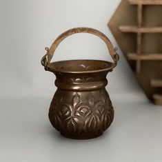 a metal pot with a handle sitting on top of a table next to some shelves