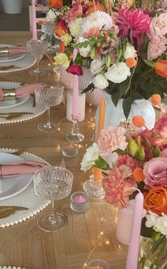 the table is set with pink and white flowers in vases, candles, and plates