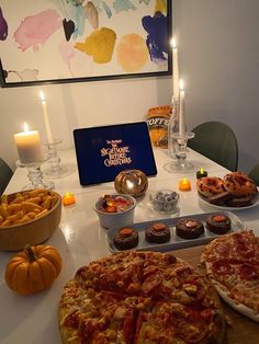 two pizzas sitting on top of a table next to plates of food and candles