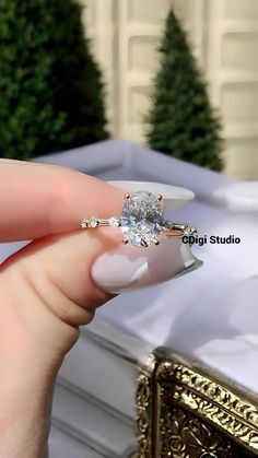 a woman's hand holding an engagement ring in front of a white box with christmas trees