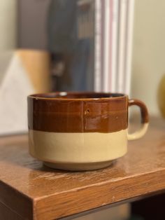 a brown and white coffee cup sitting on top of a wooden table next to an apple