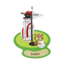 a christmas ornament with a golf ball and tee on the green grass, next to it's name