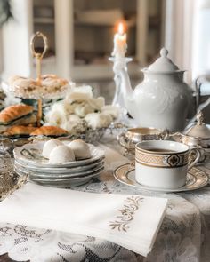 a table topped with plates and cups filled with food next to a tea pot on top of a lace covered table cloth