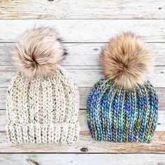 two knitted hats with pom - poms on top of wooden planks