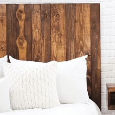 a bed with white linens and wooden headboard made from pallet wood, in front of a brick wall