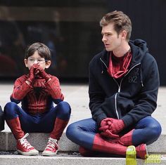 a man sitting on the ground next to a little boy wearing spider - man costumes