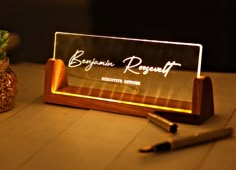 an illuminated business card holder with pen and plant next to it on a wooden table