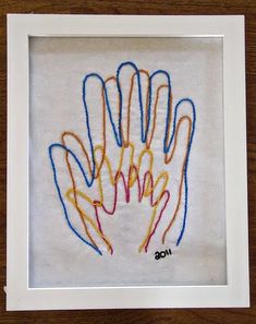 an embroidered handprint in a white frame on a wooden table with a brown background