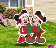 two mickey and minnie mouses standing in front of a house with christmas decorations on the lawn