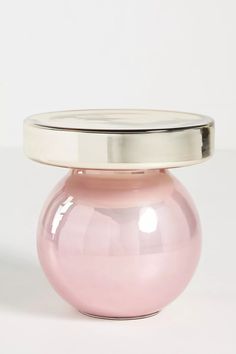 a pink vase sitting on top of a white table next to a metal container with a silver lid