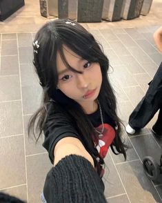 a girl with long black hair pointing her finger at the camera while standing on a tiled floor