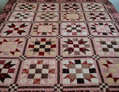 a bed with a pink and brown quilt on it's side, next to a white wall