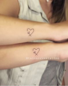 two women with matching tattoos on their arms, one has a heart and the other has a cross