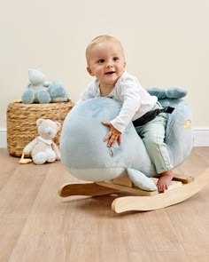 a baby is sitting on a blue whale shaped rocking toy with teddy bears in the background