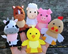 a hand holding several small felt animals in different colors and sizes, including a chicken, cow, pig, sheep, duck, horse, and giraffe